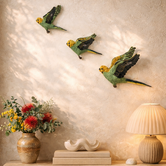 Decorative wall art of parrots above a table with a lamp and flowers.