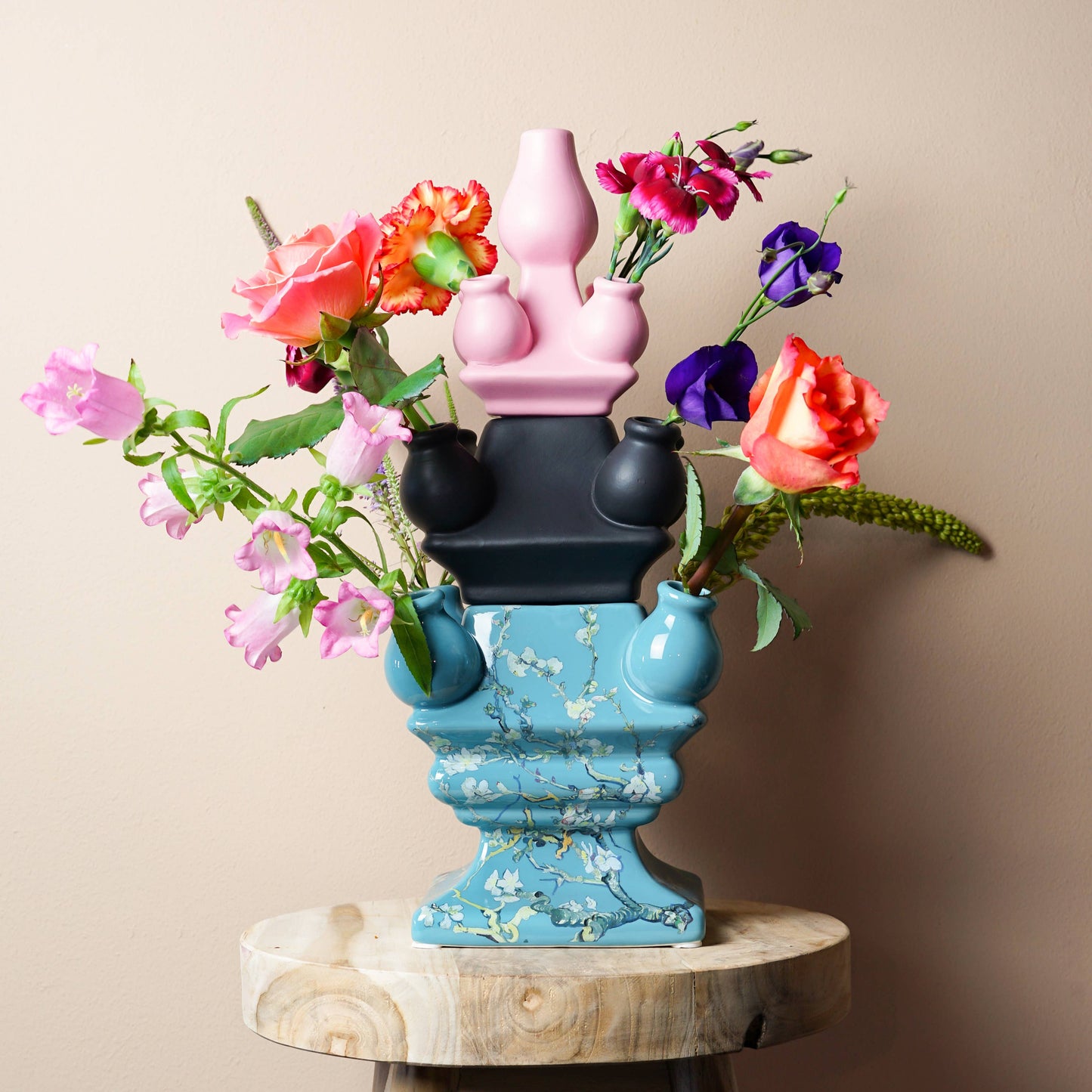Colorful vase with flowers on a wooden stool against a beige wall