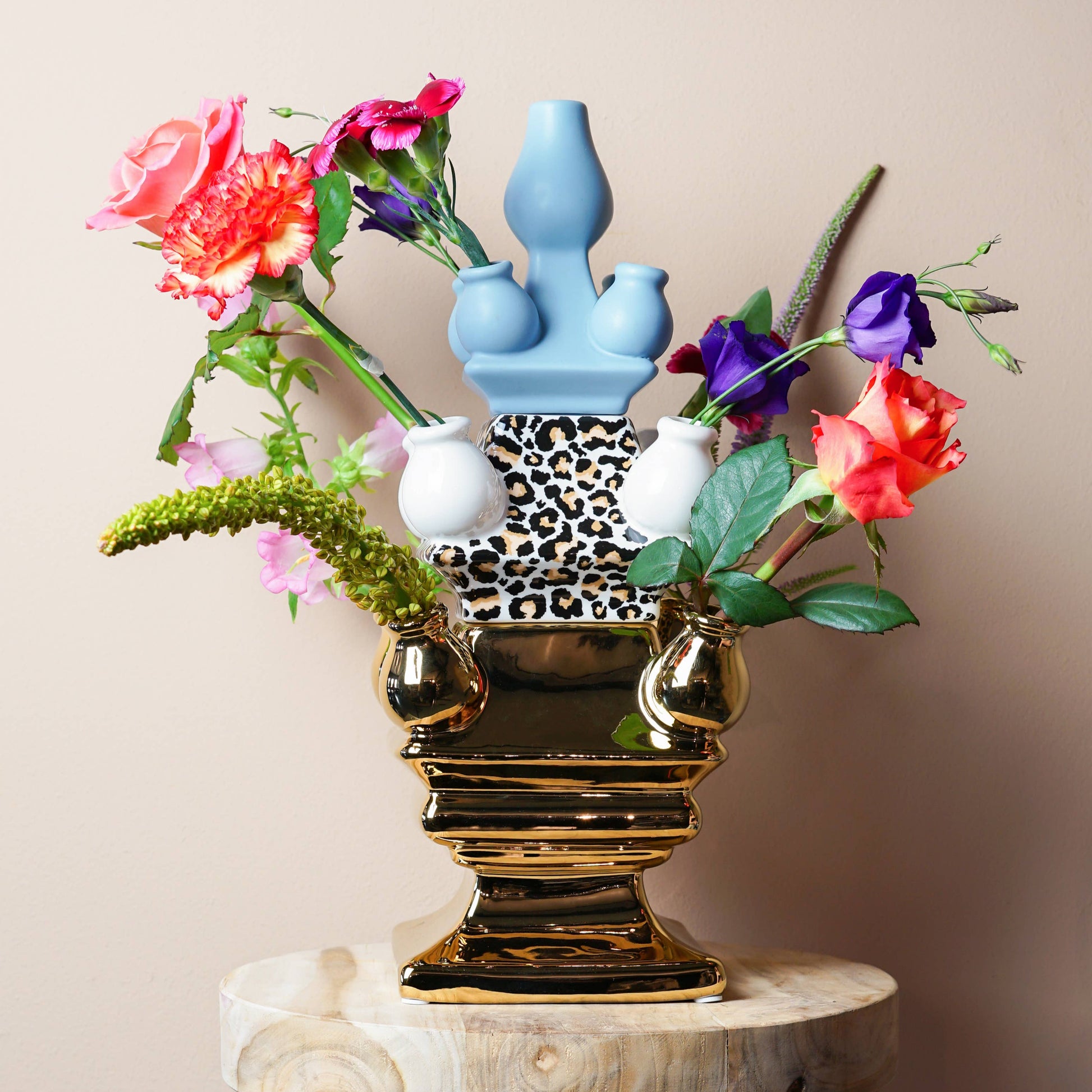 Decorative vase with colorful flowers on a wooden stool against a beige wall