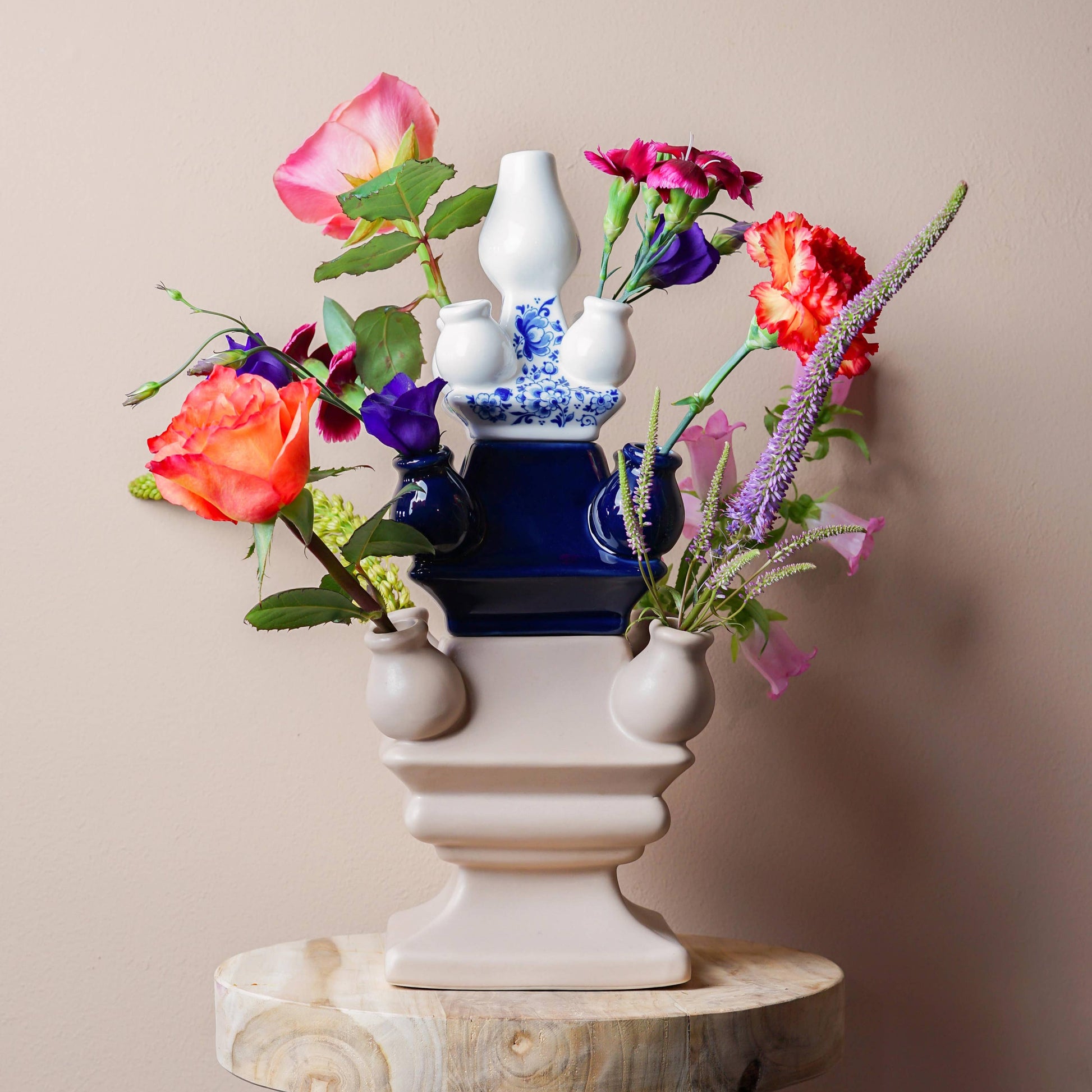 Decorative vase with colorful flowers on a wooden stool against a beige wall