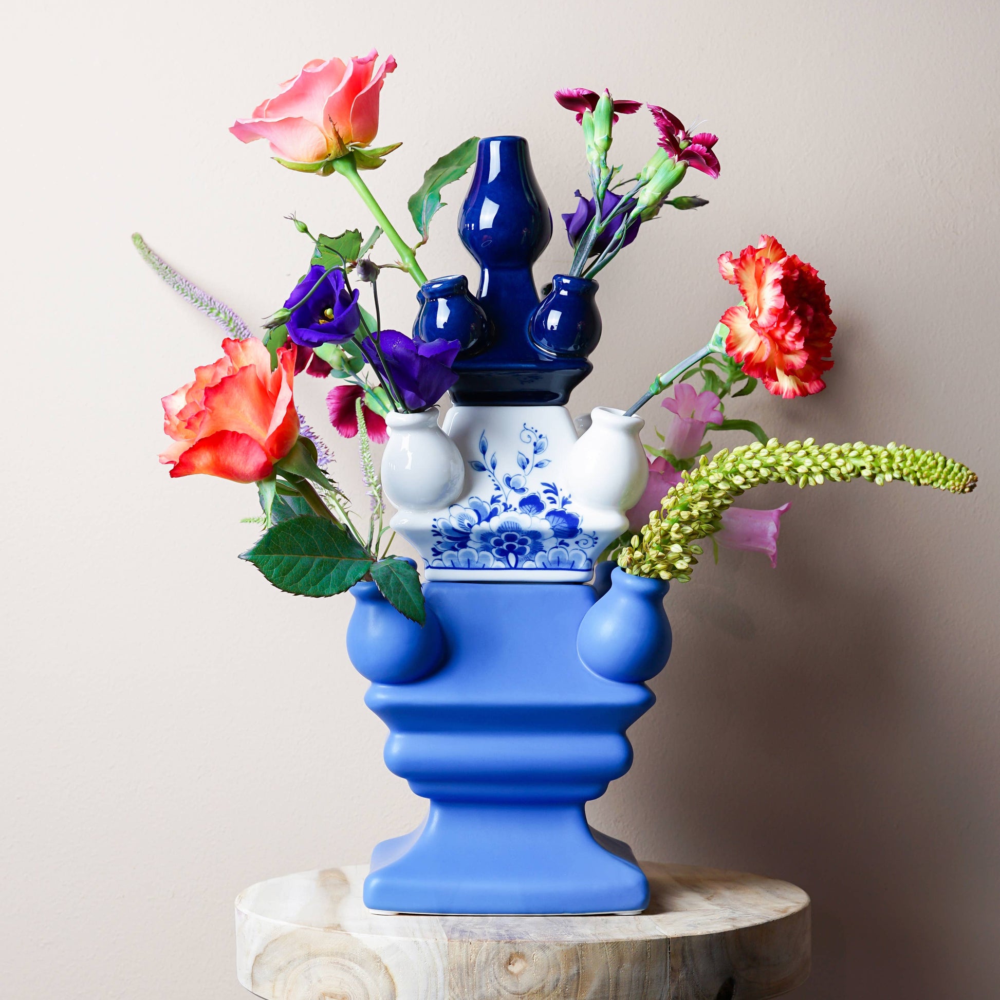 Colorful floral arrangement in a blue and white vase on a wooden stool against a plain background