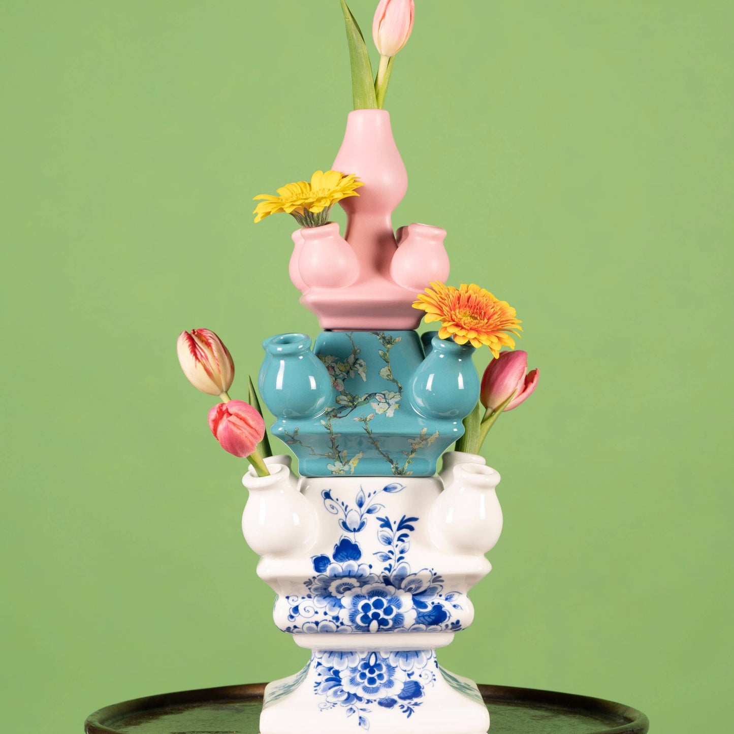 Stack of colorful ceramic vases with flowers on a green background